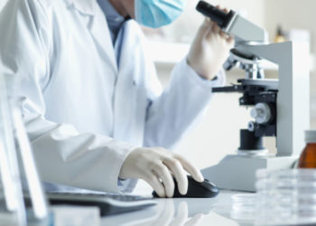 Scientist conducting research looking through microscope with computer selective focus