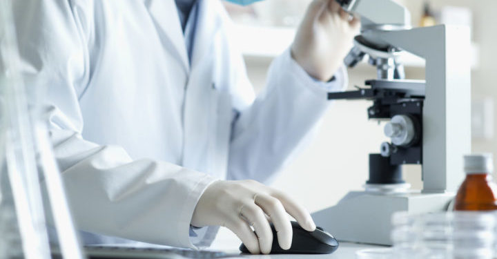 Scientist conducting research looking through microscope with computer selective focus