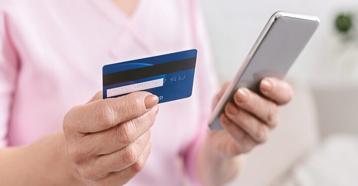 Senior woman shopping online on smartphone, paying with credit card, closeup