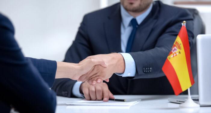 Spanish boss signing employment contract with immigrant employee, shaking hand